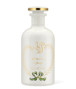A clear glass bottle of GUCCI Winter's Spring Eau De Parfum with a white label, gold accents, and a squirrel emblem.
