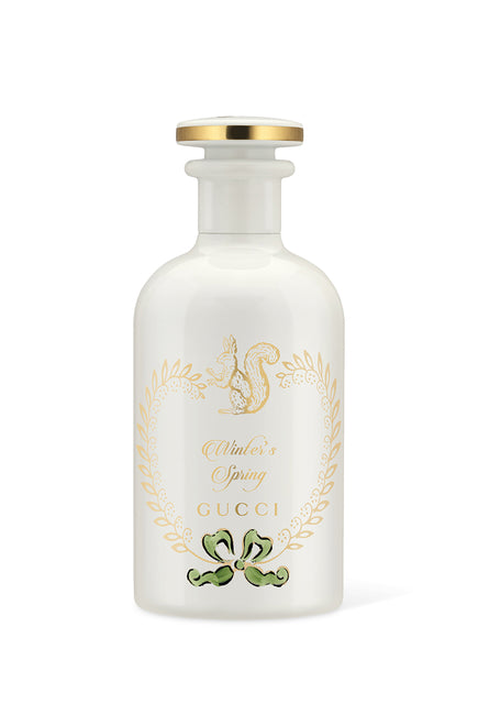 A clear glass bottle of GUCCI Winter's Spring Eau De Parfum with a white label, gold accents, and a squirrel emblem.